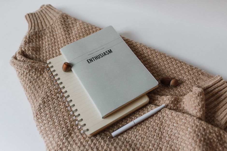 Neutral-toned flatlay featuring a notebook, sweater, and pen; perfect for inspiration or cozy themes.