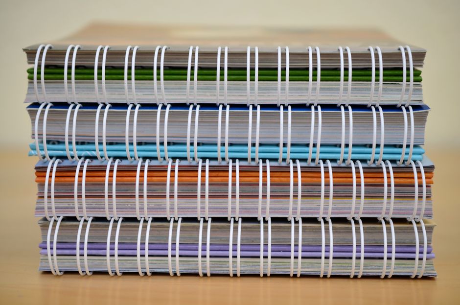 A stack of colorful spiral-bound notebooks placed on a wooden table, showcasing various colors and designs.